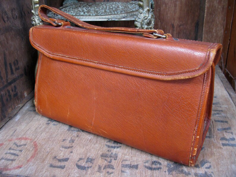 May include: A brown leather handbag with a flap closure and a short handle. The bag has a worn, vintage look.