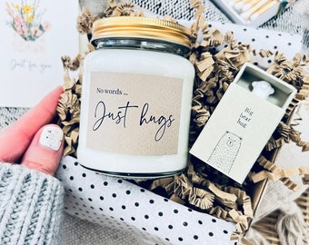 May include: A gift box filled with brown packing paper and white polka dot paper. The box contains a white candle in a glass jar with a gold lid and a brown label that says "No words... Just hugs". There is also a small white box with a bear illustration and the text "Big bear hug".