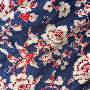 Puede incluir: Primer plano de una tela azul marino con un estampado floral. El diseño presenta grandes flores blancas con centros y acentos rojos, junto con hojas y tallos rojos. El patrón se repite en la tela.