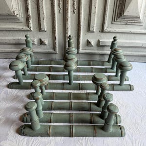 May include: A collection of four horizontal wall-mounted coat racks made of wood with a distressed sage green finish. Each rack features a bamboo-style design with three evenly spaced pegs topped with rounded knobs for hanging garments.