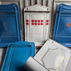 Può includere: Una collezione di cinque unità di stoccaggio a parete in metallo smaltato vintage. Tre sono blu tinta unita, una è bianca con un motivo a quadri rossi e una è bianca con bordi dorati. Ognuna presenta un retro piatto, un ripiano e una barra.