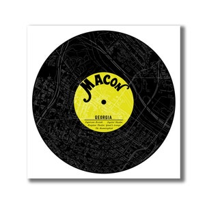 May include: A black and white map of Macon, Georgia, is displayed on a vinyl record. The record is yellow with the word "MACON" in black lettering. The text "GEORGIA" is below the word "MACON" along with a list of local businesses.