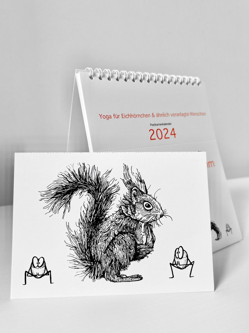 Der Kalender Yoga für Eichhörnchen & ähnlich veranlagte Menschen, Postkartenkalender 2024 steht aufgeklappt auf einer weißen Fläche.Im Vordergrund eine abgetrennte Postkarte.