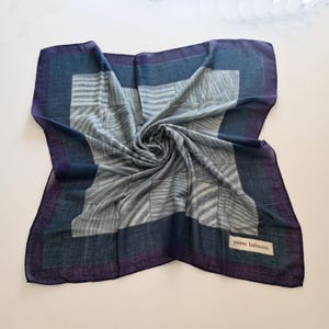 Peut inclure: Un foulard carré avec un motif géométrique dans les tons de bleu, gris et violet. Le foulard a une bordure dans des tons plus foncés de bleu et de violet. Le nom de la marque "pierre balmain" est visible sur une petite étiquette.