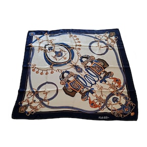 May include: Square silk scarf with a cream background, navy blue border, and intricate equestrian-themed design. The scarf features gold, navy, and brown details, including horse tack and chain patterns. The scarf has the text "Sorelle Fontana" in the bottom right corner.