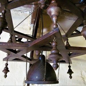 May include: A wooden chandelier with a star-shaped frame and multiple hanging wooden finials. The chandelier has a dark brown finish and is suspended from the ceiling by chains.