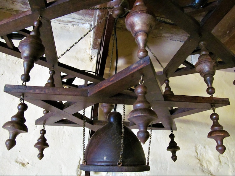 May include: A wooden chandelier with a star-shaped frame and multiple hanging wooden finials. The chandelier has a dark brown finish and is suspended from the ceiling by chains.