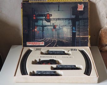 Puede incluir: Juego de tren modelo Jouef a escala HO vintage, con una caja que muestra una escena ferroviaria y el texto "THIONVILLE TRAFIC". El juego incluye vías, vagones y una locomotora, todo en una bandeja color crema.