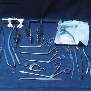 Può includere: Un set di strumenti chirurgici, tra cui pinze, clamp, forbici e un porta-aghi. Gli strumenti sono realizzati in acciaio inossidabile e hanno una finitura lucida. Alcuni degli strumenti sono confezionati in un sacchetto di plastica trasparente.