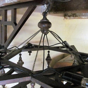 May include: A wooden chandelier with a star-shaped frame and multiple light bulbs. The chandelier is suspended from the ceiling by chains and wires.