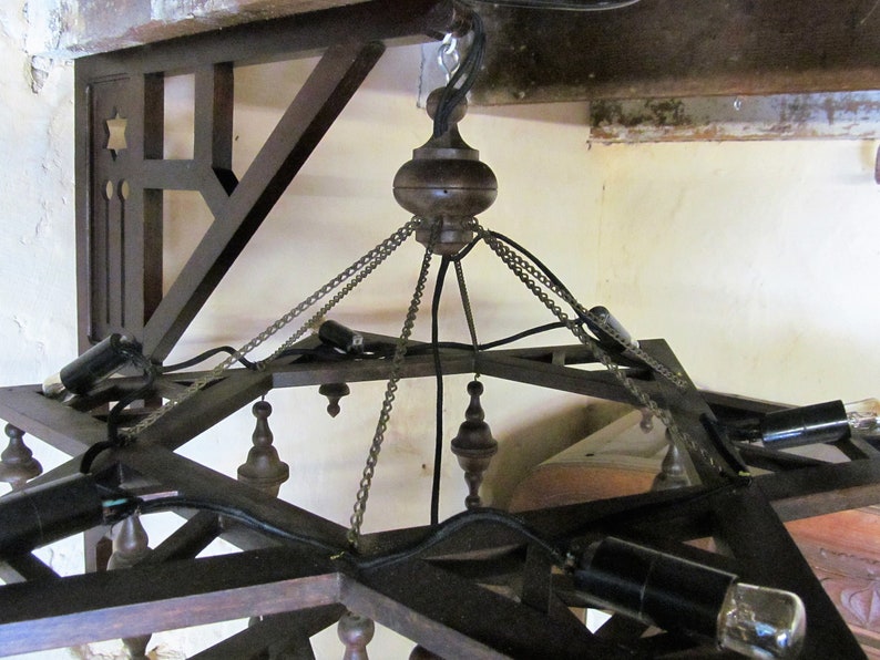 May include: A wooden chandelier with a star-shaped frame and multiple light bulbs. The chandelier is suspended from the ceiling by chains and wires.