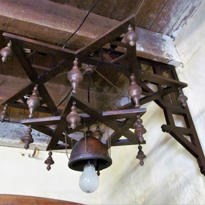 May include: A wooden star-shaped chandelier with a bell-shaped light fixture and multiple dangling wooden ornaments. The chandelier is mounted to a wooden beam.