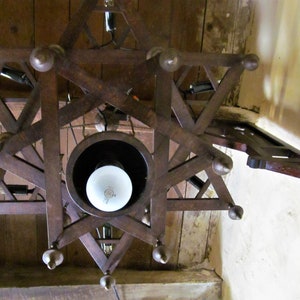 May include: A wooden star-shaped chandelier with a white light bulb in the center. The chandelier is hanging from a wooden ceiling.