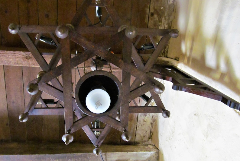 May include: A wooden star-shaped chandelier with a white light bulb in the center. The chandelier is hanging from a wooden ceiling.