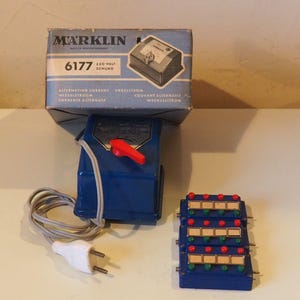 May include: A vintage Marklin 6177 transformer set with a blue and red control box, a blue control panel with red and green lights, and a box with text. The set includes a white plug and a gray cord.