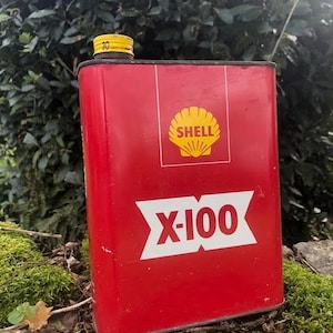 Puede incluir: Una lata de metal roja con un logotipo de Shell amarillo y el texto "X-100".
