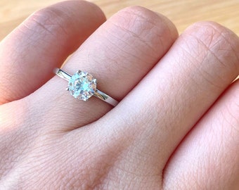 May include: A silver ring with a clear round gemstone.