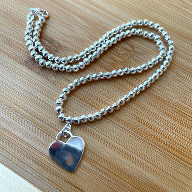 May include: A silver necklace with a heart-shaped pendant. The necklace is made of small, round beads.