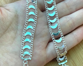 May include: Two silver chains with a crescent moon design. The chains are layered on top of each other and are held in a hand.