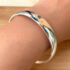 May include: A shiny silver bangle bracelet with a smooth, rounded surface.