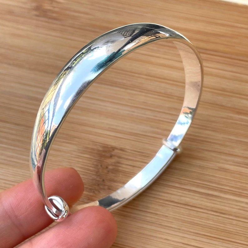 May include: A silver bangle bracelet with a smooth, polished finish. The bracelet is open and has a hinged clasp.