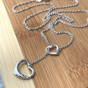 May include: A silver necklace with two open heart pendants. The necklace is on a wooden surface.