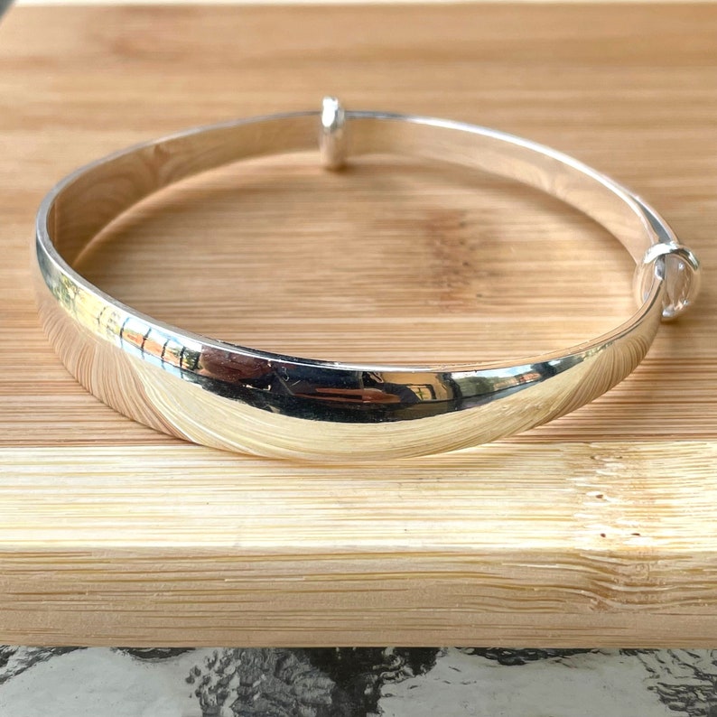 May include: A silver bangle bracelet with a smooth, polished finish. The bracelet is open and has a hinged clasp.