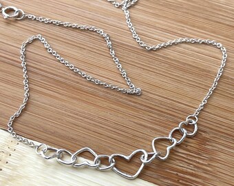 May include: A silver necklace with a chain and a pendant made of interconnected heart shapes.