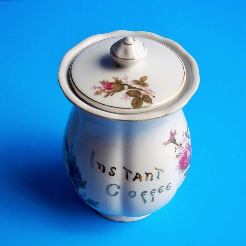 A lovely vintage Lipper & Mann coffee container with lid. It has Instant Coffee in gold letters on front. This coffee canister has a pompadour rose design which would be great for a French Country Cottage décor kitchen. Lid with rose pattern and gold trim. 6 1/2" High 3 1/2" Wide 5" Depth the lid fits nicely, (has cork around base of lid to seal when closed), Sold as Found; will need to be cleaned; has a few areas where discoloration are like specks and could have occurred during creation.