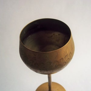 A 12" tall brass goblet.
This is a vintage brass goblet with a leaf etched design around the bowl and the base. 
The bottom of the goblet bowl is not smooth and the bottom goes into the stem a little bit so it's not recommended to drink out of it. 
Great for many styles of décor such as bohemian, farmhouse, romantic or cottage.  
approx. 
12" Tall
4 1/2-3/4" at widest point
3 3/4" opening
4 1/2" depth
base is 4 3/4" diameter
3/8" width at middle of stem
India is etched on bottom