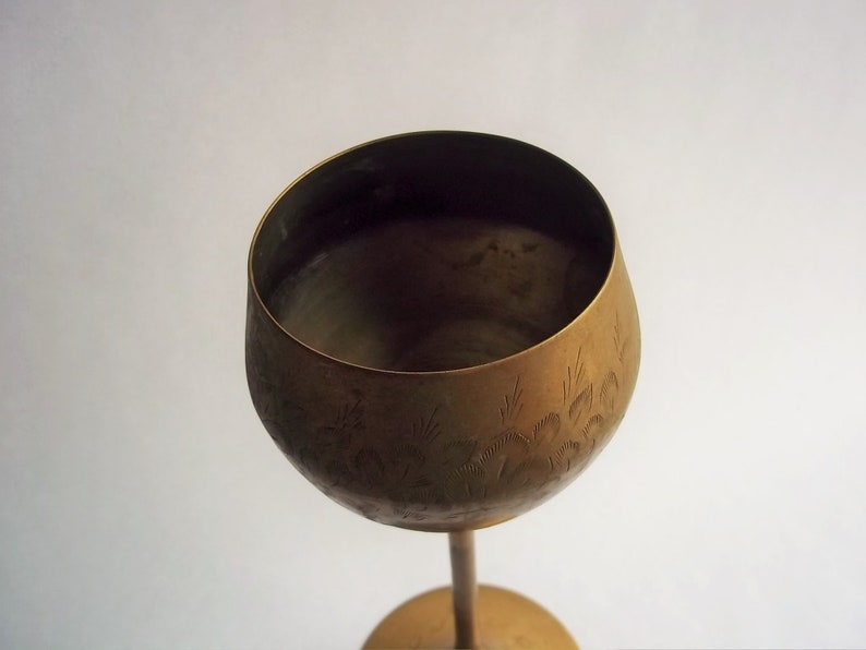 A 12" tall brass goblet.
This is a vintage brass goblet with a leaf etched design around the bowl and the base. 
The bottom of the goblet bowl is not smooth and the bottom goes into the stem a little bit so it's not recommended to drink out of it. 
Great for many styles of décor such as bohemian, farmhouse, romantic or cottage.  
approx. 
12" Tall
4 1/2-3/4" at widest point
3 3/4" opening
4 1/2" depth
base is 4 3/4" diameter
3/8" width at middle of stem
India is etched on bottom