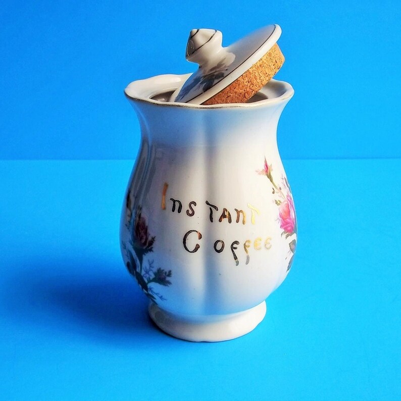 A lovely vintage Lipper & Mann coffee container with lid. It has Instant Coffee in gold letters on front. This coffee canister has a pompadour rose design which would be great for a French Country Cottage décor kitchen. Lid with rose pattern and gold trim. 6 1/2" High 3 1/2" Wide 5" Depth the lid fits nicely, (has cork around base of lid to seal when closed), Sold as Found; will need to be cleaned; has a few areas where discoloration are like specks and could have occurred during creation