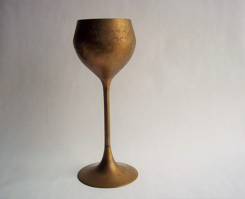 A 12" tall brass goblet.
This is a vintage brass goblet with a leaf etched design around the bowl and the base. 
The bottom of the goblet bowl is not smooth and the bottom goes into the stem a little bit so it's not recommended to drink out of it. 
Great for many styles of décor such as bohemian, farmhouse, romantic or cottage.  
approx. 
12" Tall
4 1/2-3/4" at widest point
3 3/4" opening
4 1/2" depth
base is 4 3/4" diameter
3/8" width at middle of stem
India is etched on bottom