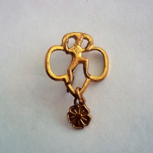 May include: Gold Girl Scout pin with a flower charm. The pin features a silhouette of a girl scout in uniform.