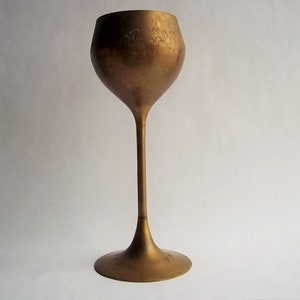A 12" tall brass goblet.
This is a vintage brass goblet with a leaf etched design around the bowl and the base. 
The bottom of the goblet bowl is not smooth and the bottom goes into the stem a little bit so it's not recommended to drink out of it. 
Great for many styles of décor such as bohemian, farmhouse, romantic or cottage.  
approx. 
12" Tall
4 1/2-3/4" at widest point
3 3/4" opening
4 1/2" depth
base is 4 3/4" diameter
3/8" width at middle of stem
India is etched on bottom