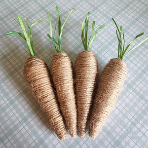 May include: Four brown twine-wrapped carrots with green paper leaves. The carrots are arranged in a fan shape on a green and white checkered surface.