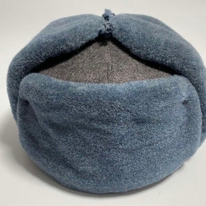 Könnte beinhalten: Eine blaue und graue Fleece-Wintermütze mit einem umklappbaren Ohrenschutz.