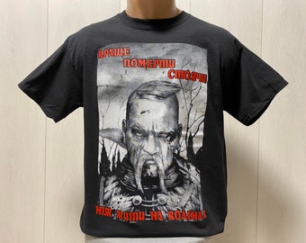 May include: Black t-shirt with a graphic print of a man with a beard and mustache. The text on the shirt reads "Краще померти стоячи ніж жити на колінах".