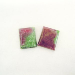May include: Two rectangular cabochon gemstones, one green and pink, the other purple and pink.
