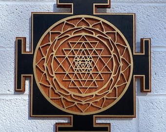 May include: A wooden wall hanging with a black background and a gold Sri Yantra design. The Sri Yantra is a geometric pattern that is considered to be a powerful symbol in Hinduism.