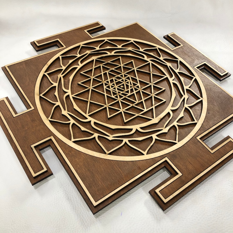 Puede incluir: Una placa cuadrada de madera marr&oacute;n con un dise&ntilde;o geom&eacute;trico en el centro. El dise&ntilde;o es un Sri Yantra, un s&iacute;mbolo sagrado en el hinduismo. La placa tiene un borde marr&oacute;n claro.