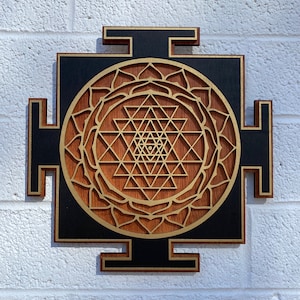 Puede incluir: Un tapiz de pared de madera con fondo negro y un dise&ntilde;o dorado de Sri Yantra. El Sri Yantra es un patr&oacute;n geom&eacute;trico que se considera un s&iacute;mbolo poderoso en el hinduismo.