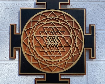 May include: A wooden wall hanging with a black background and a gold Sri Yantra design. The Sri Yantra is a geometric pattern that is considered to be a powerful symbol in Hinduism.