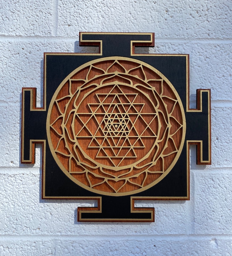 Puede incluir: Un tapiz de pared de madera con fondo negro y un dise&ntilde;o dorado de Sri Yantra. El Sri Yantra es un patr&oacute;n geom&eacute;trico que se considera un s&iacute;mbolo poderoso en el hinduismo.