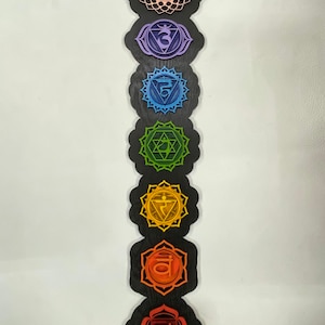 May include: A wooden wall hanging with seven colorful chakra symbols, each with a different Sanskrit symbol and a lotus flower at the top and bottom.