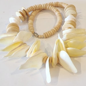 May include: A cream-colored necklace featuring a variety of natural elements. The necklace includes large, petal-shaped shell pieces, wooden beads, and smaller, round wooden elements. The necklace is approximately 18 inches long and has a silver clasp.