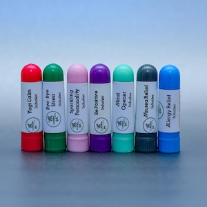 May include: Eight small, colourful, cylindrical aromatherapy inhalers with white labels. The labels have the names of the scents and the word "Inhaler" printed on them. The scents are: Yogi Calm, Bye-Bye Stress, Sparkling Personality, Be Positive, Mind Opener, Nausea Relief, and Allergy Relief.