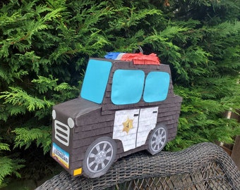May include: A black police car pinata with blue windows, a white star, and the number 4. The pinata is decorated with red and white streamers.