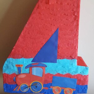 May include: A red and blue number four piñata shaped like a train. The train has a blue roof, red body, and black wheels. The piñata is decorated with blue and turquoise tissue paper.