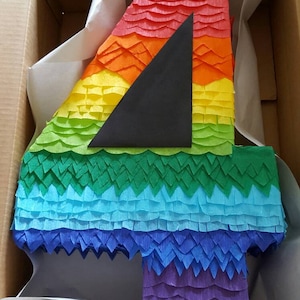 May include: A rainbow-colored pinata shaped like the number four. The pinata is made of tissue paper and has a black triangle in the center.